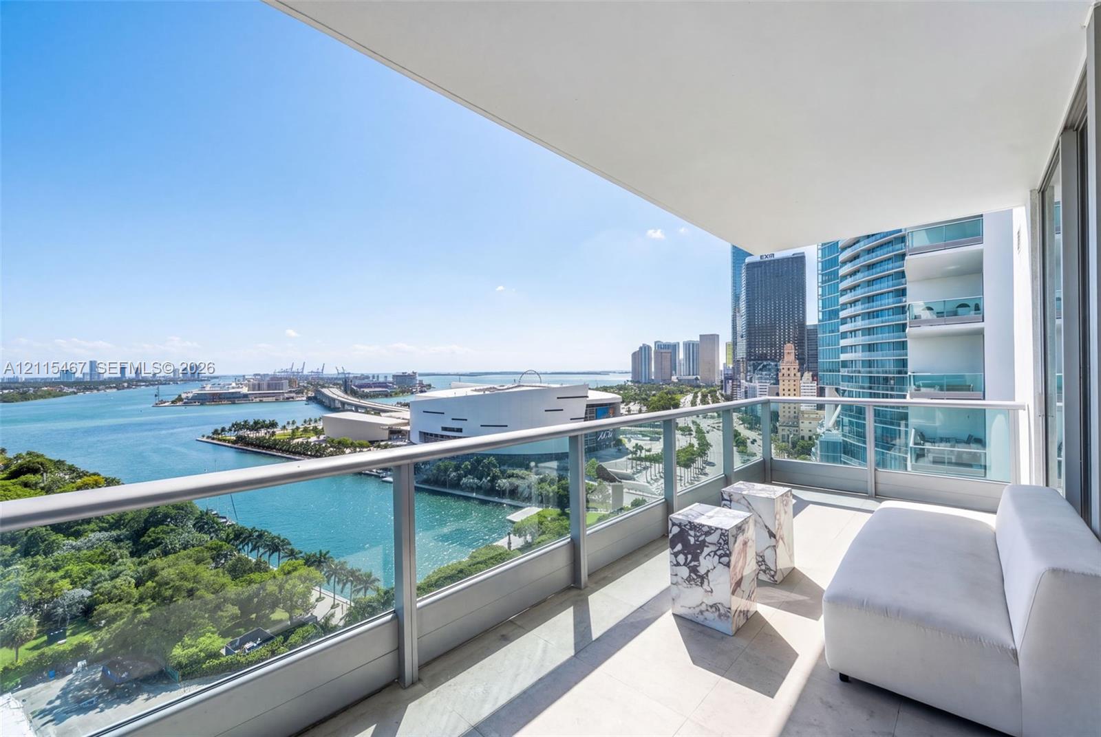 Covered balcony with a glass and metal railing, concrete flooring, and water and urban skyline backdrop
