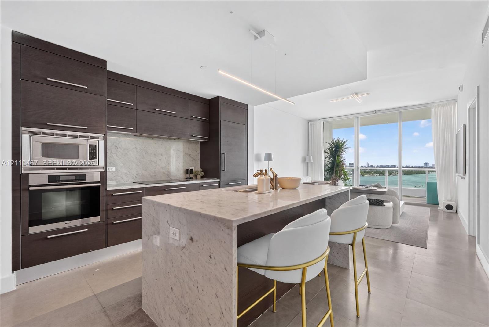 Modern kitchen featuring flat-panel cabinetry, stone countertops, integrated stainless steel appliances, a waterfall-edge island, and floor-to-ceiling glass doors