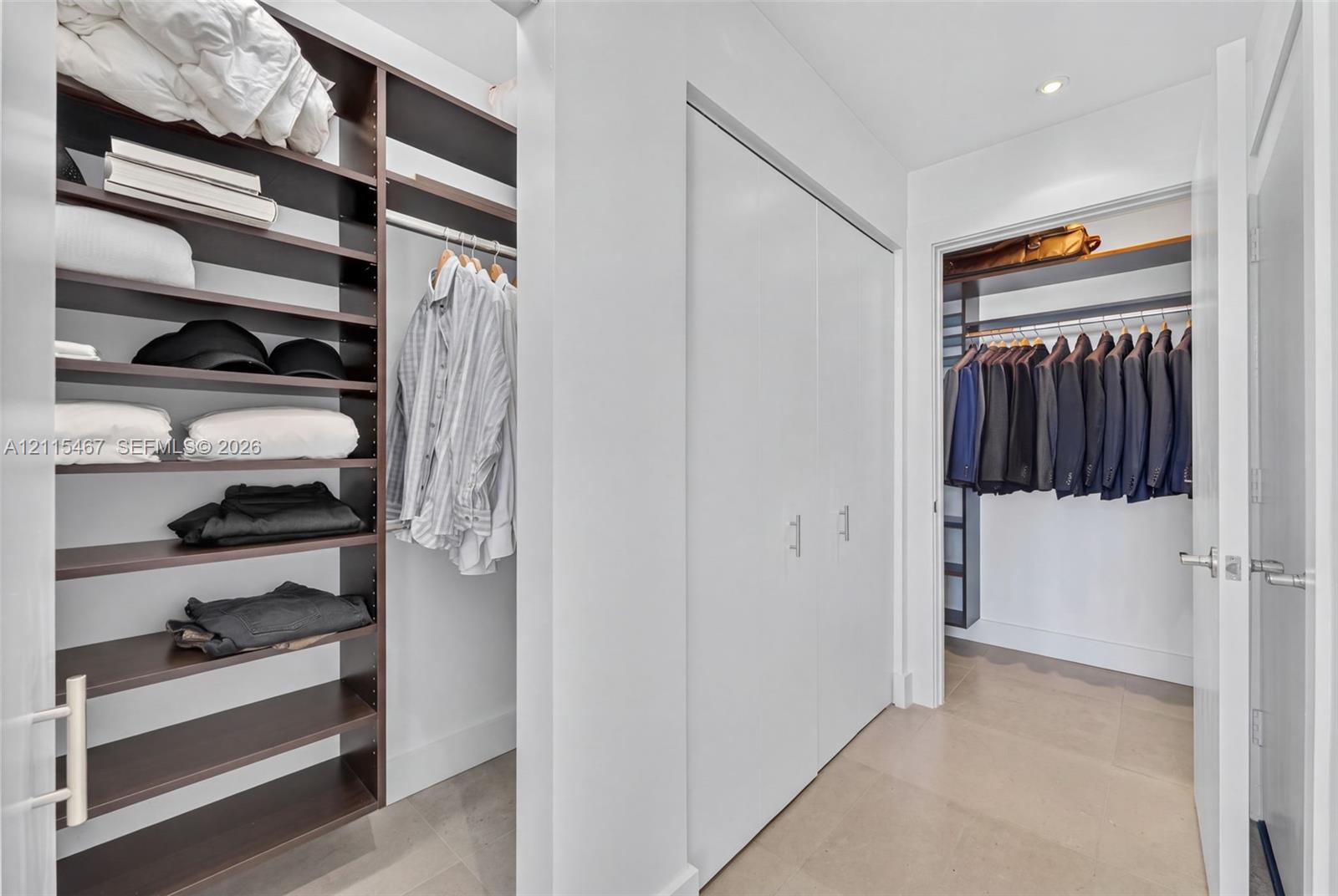 Custom closet organization system featuring dark wood-finish open shelving, built-in hanging rods, and white double-door cabinetry with metallic hardware