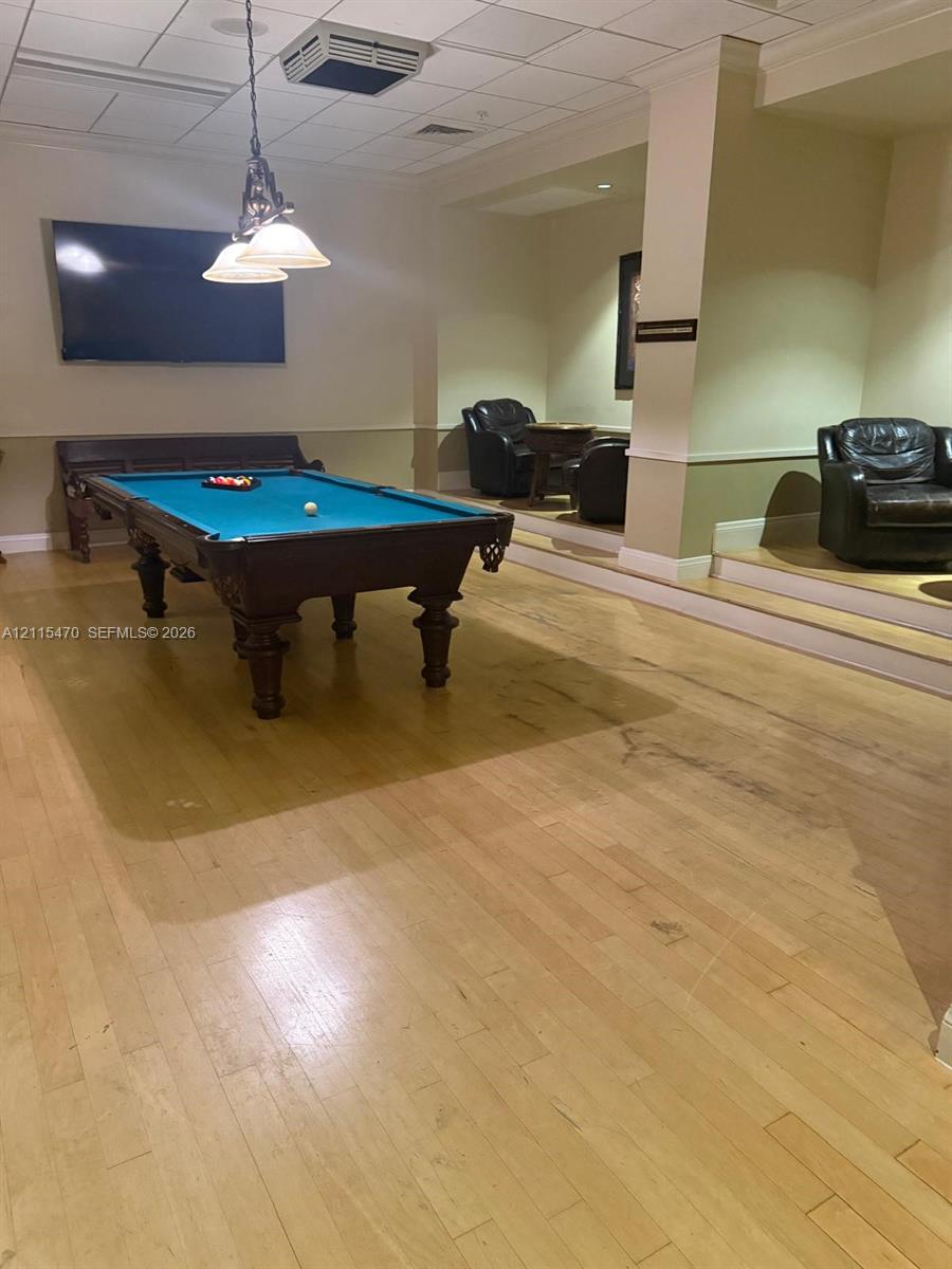 Spacious recreation room featuring wood-finish flooring, a raised platform seating area, and a multi-pendant light fixture