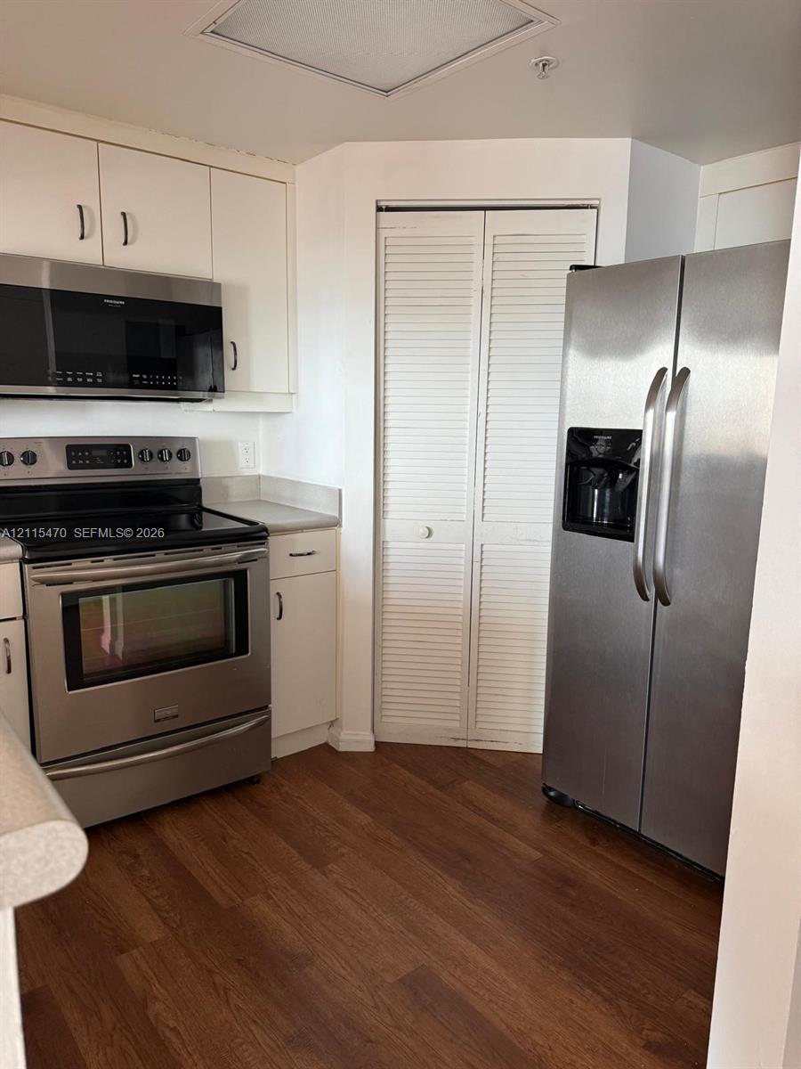 Kitchen featuring stainless steel appliances, wood-finish flooring, white cabinetry, and a bi-fold closet door