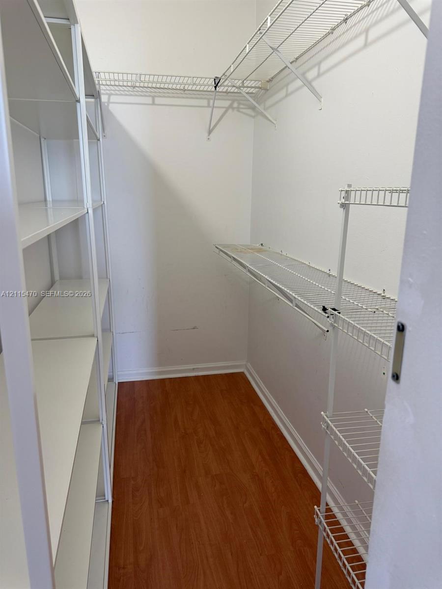 Walk-in closet featuring wood-finish flooring, white solid shelving, and white wire rack shelving