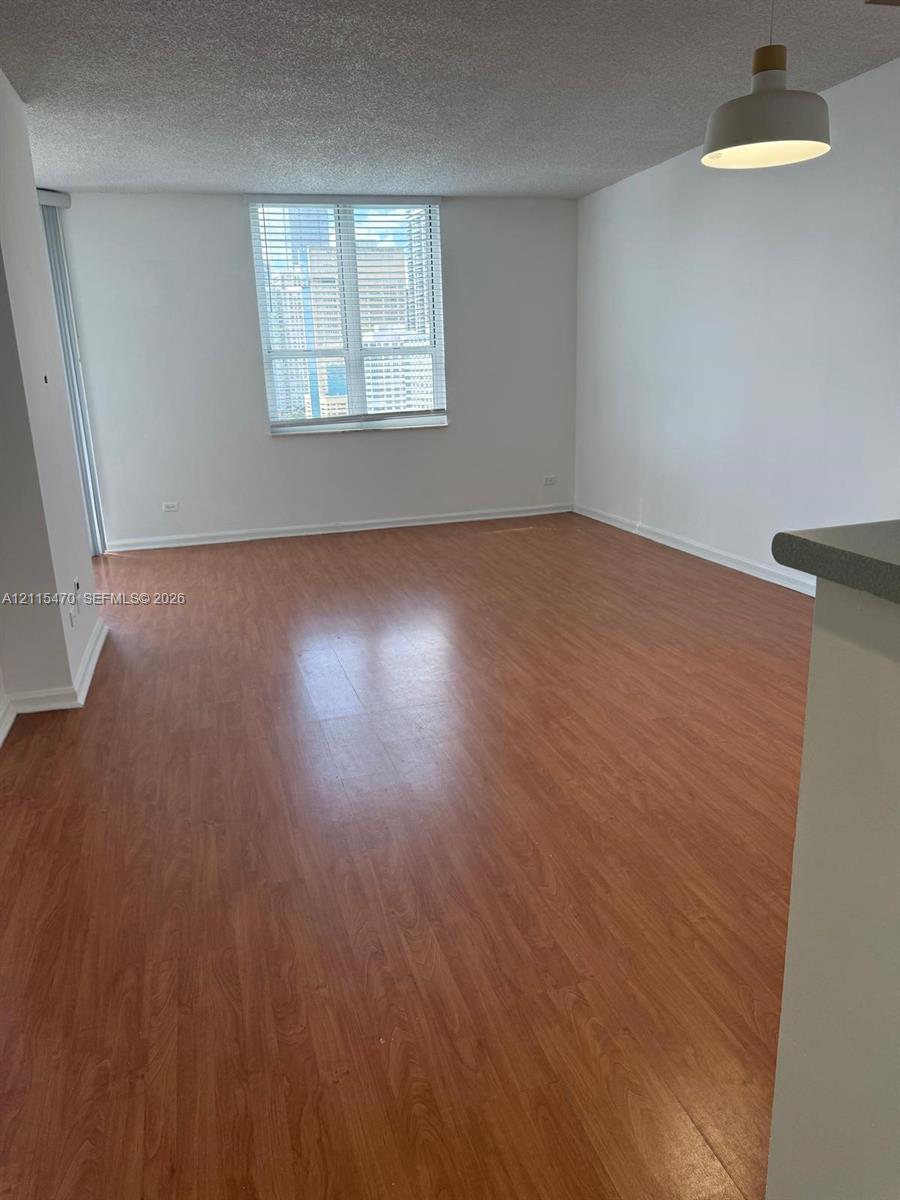 Open living area featuring wood-finish flooring, a large window with horizontal blinds, neutral wall paint, and a pendant light fixture