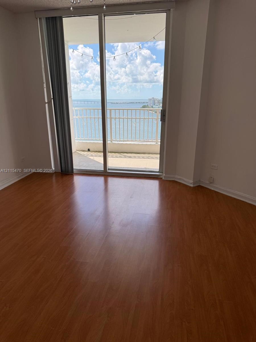 Wood-finish flooring, sliding glass door, and covered balcony with metal railing overlooking the water