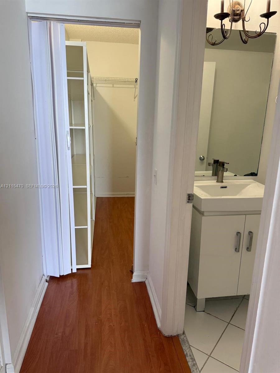 Walk-in closet featuring white built-in shelving, complemented by a vanity area with a white cabinet, square sink, wall-mounted mirror, and ceramic tile flooring