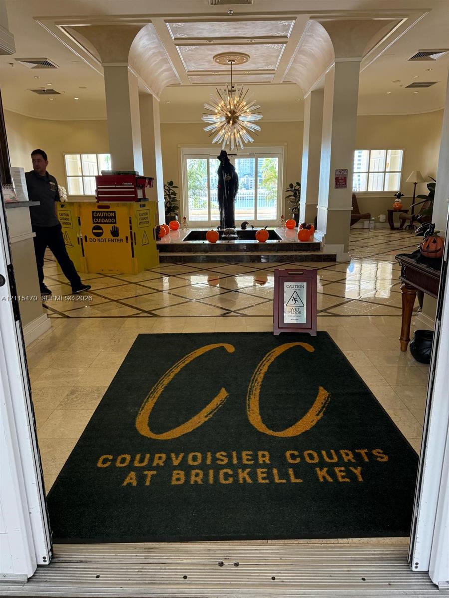 Grand lobby entrance featuring stone tile flooring with decorative inlay, a coffered ceiling, a multi-arm sputnik chandelier, and a central tiered platform