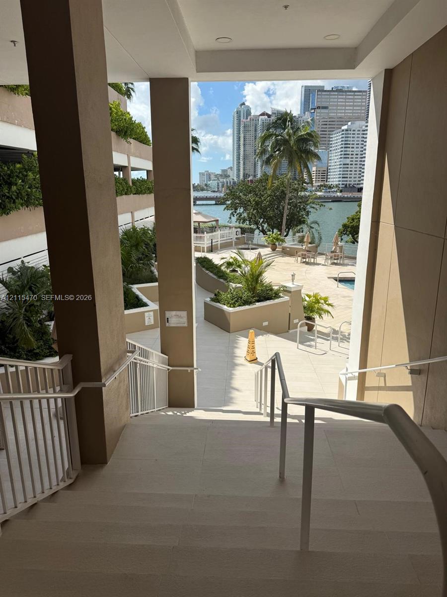 Covered concrete staircase with white metal railings, leading to an outdoor terrace featuring hardscaped planters, integrated landscaping, and proximity to the waterfront