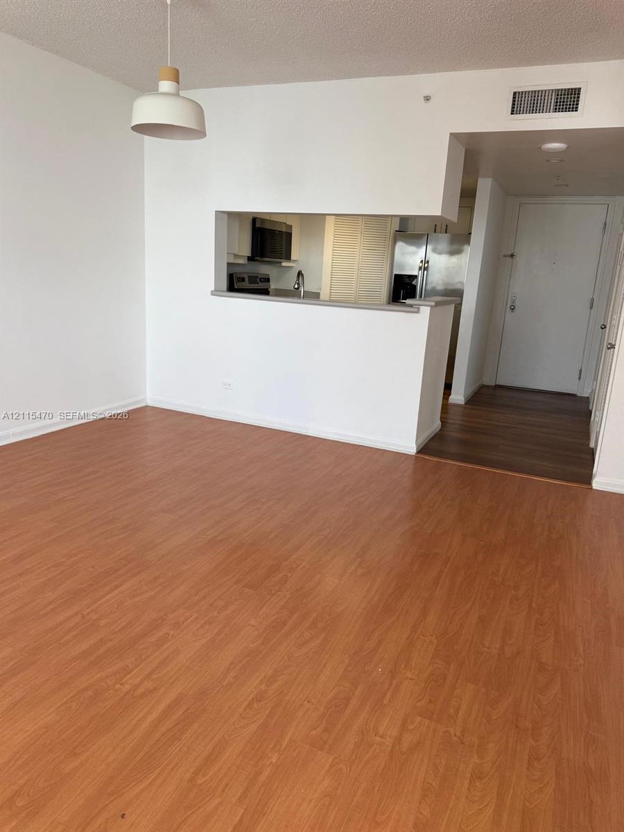 Open floor plan featuring wood-finish flooring, a pass-through kitchen opening, stainless steel appliances, and a minimalist pendant light fixture