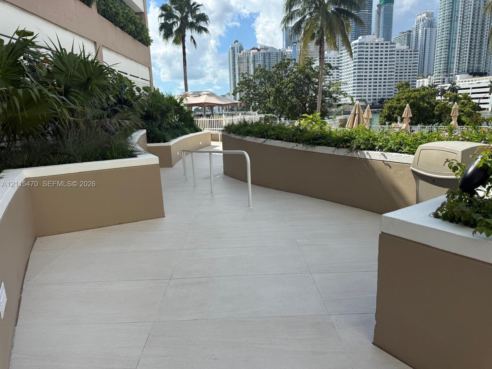 Outdoor terrace featuring large-format tile flooring, perimeter planters with mature greenery, and a white metal safety railing