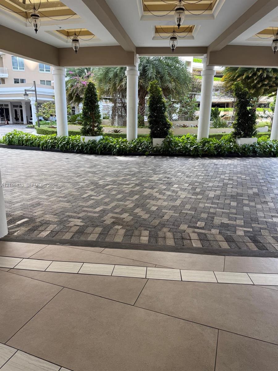 Covered portico entrance featuring structural columns, recessed lighting, and a paved motor court with formal landscaping