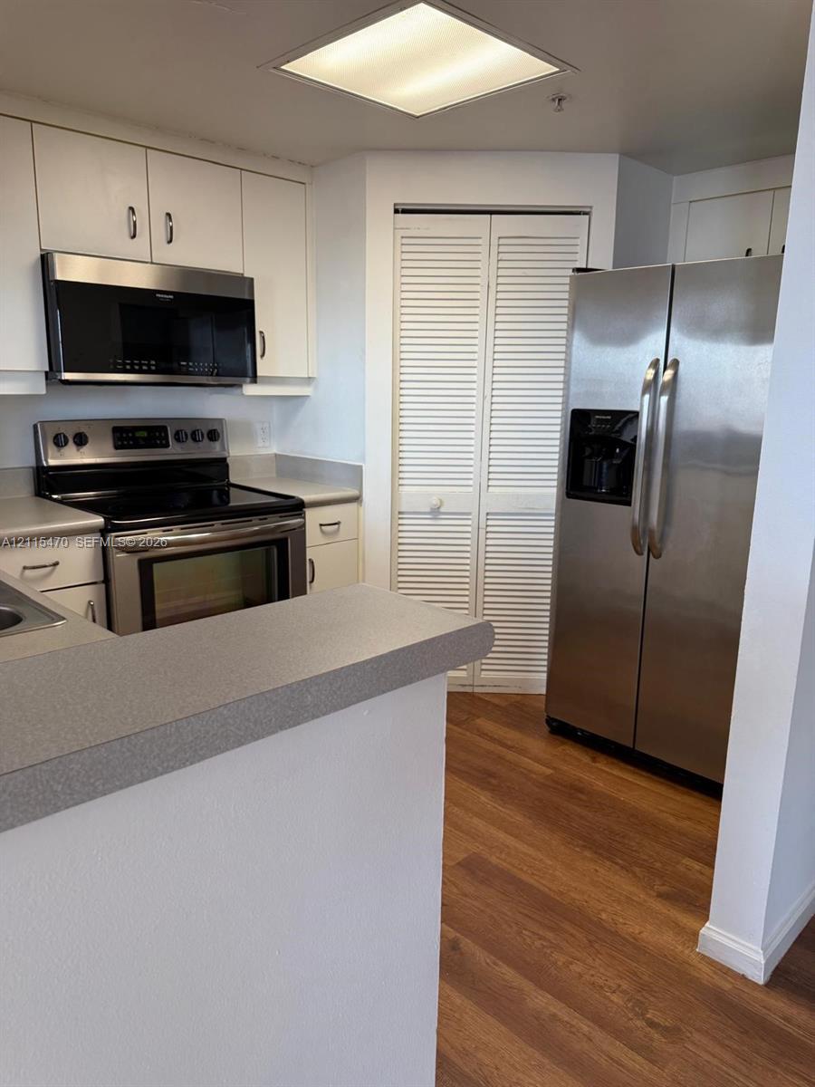 Kitchen featuring white cabinetry, wood-finish flooring, stainless steel appliances, solid-surface countertops, and louvered-door pantry storage