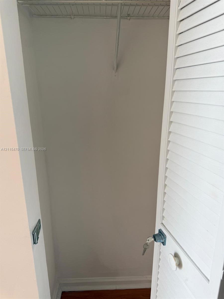 Storage closet featuring a white louvered door, a built-in wire shelf, a metal hanging rod, and a locking knob