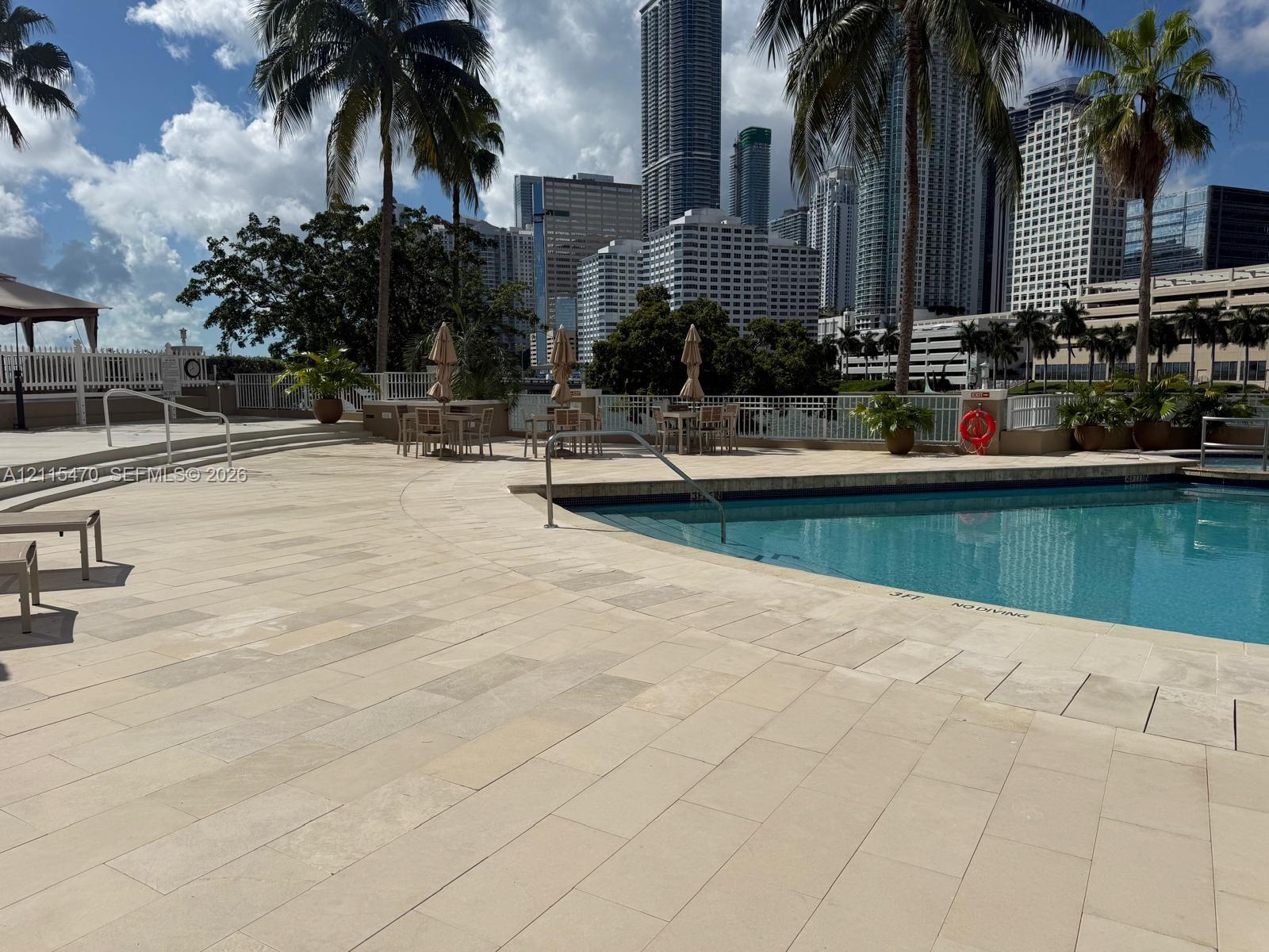 Swimming pool with stone-tiled decking, metal safety railing, and mature palm trees
