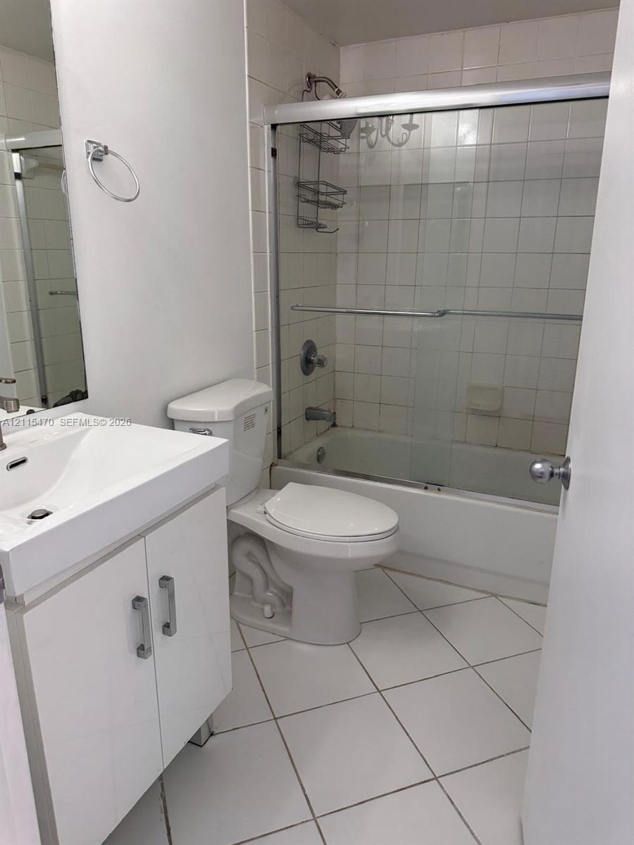 Full bathroom featuring a white vanity cabinet with a rectangular sink, porcelain tile flooring, and a shower-tub combination enclosed by sliding glass doors