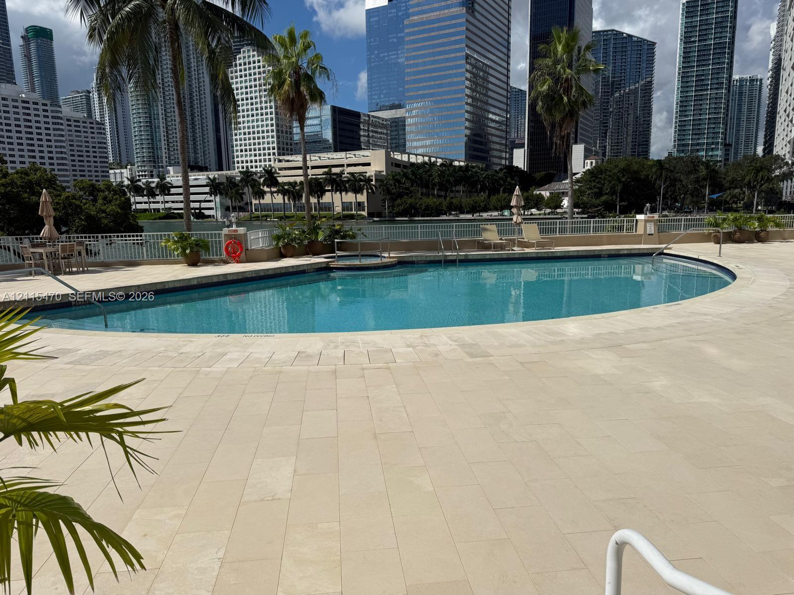 Curved swimming pool with stone-tile surround, integrated spa, metal perimeter railing, and palm tree landscaping