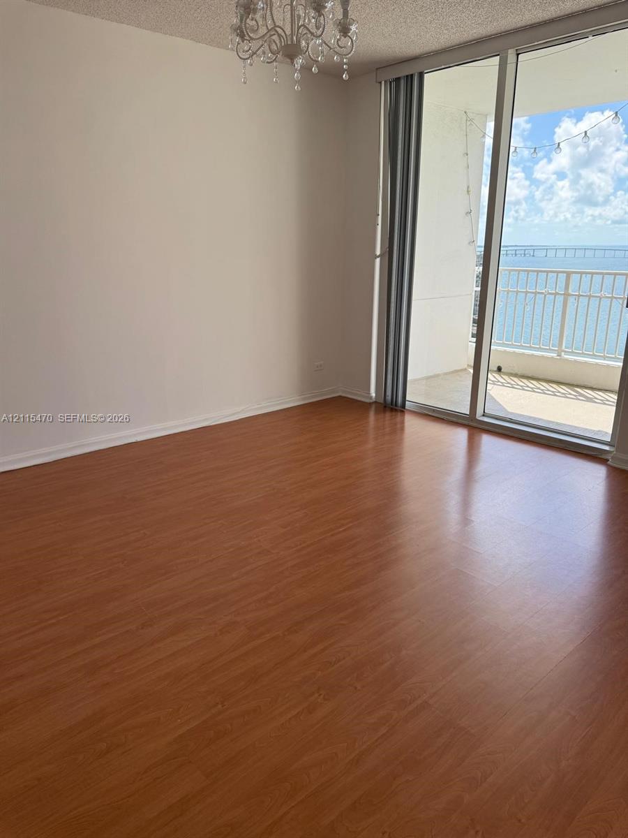 Wood-finish flooring, floor-to-ceiling glass doors, private balcony, and decorative chandelier