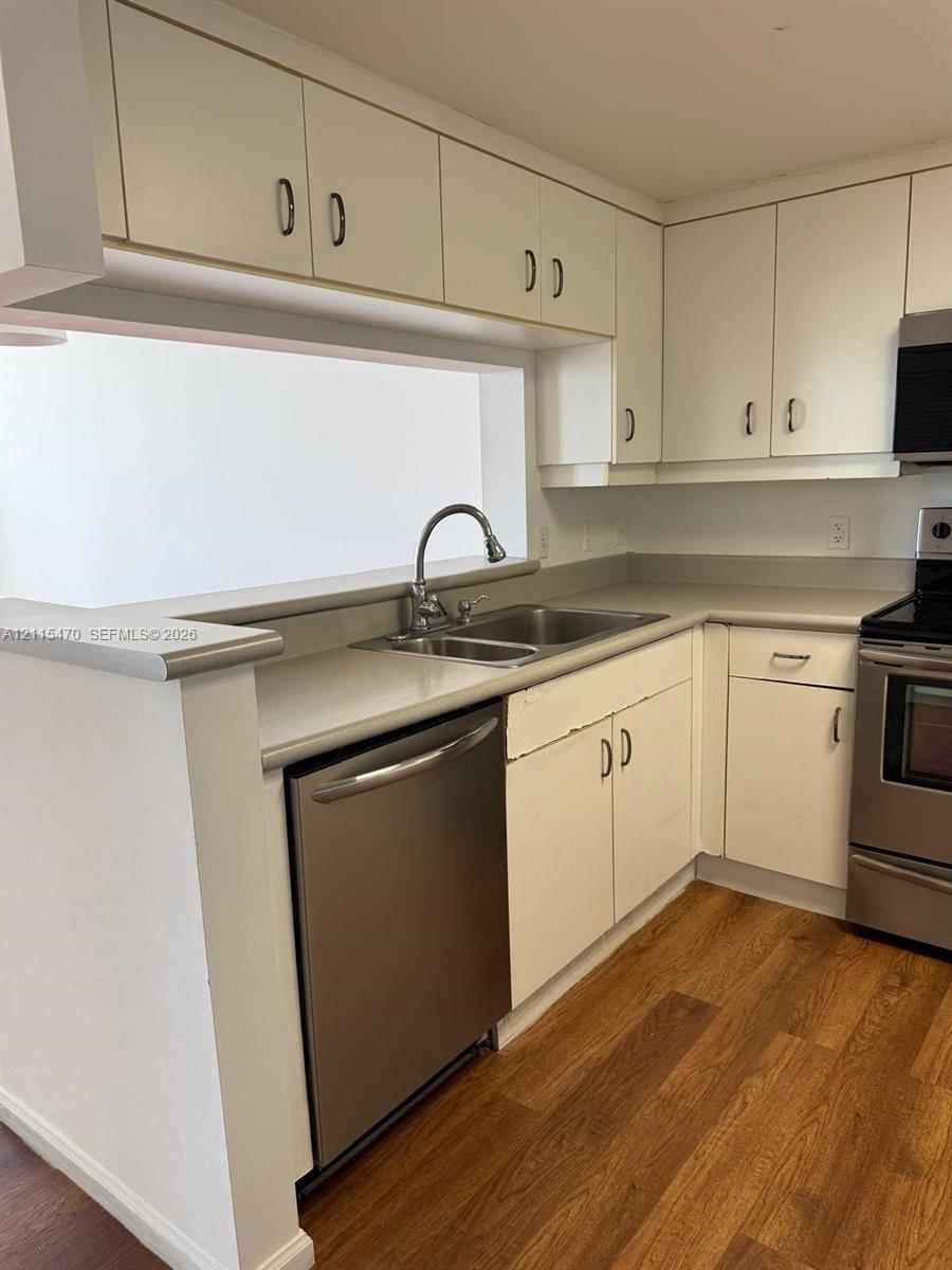 Kitchen featuring stainless steel appliances, wood-finish flooring, white cabinetry, and a double-basin undermount sink