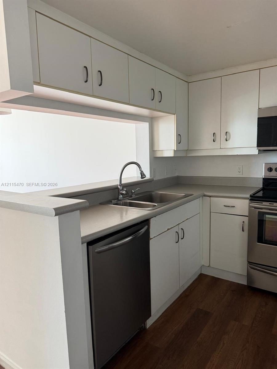 Kitchen featuring white cabinetry, stainless steel appliances, dual-basin sink with a gooseneck faucet, solid-surface countertops, and wood-finish flooring