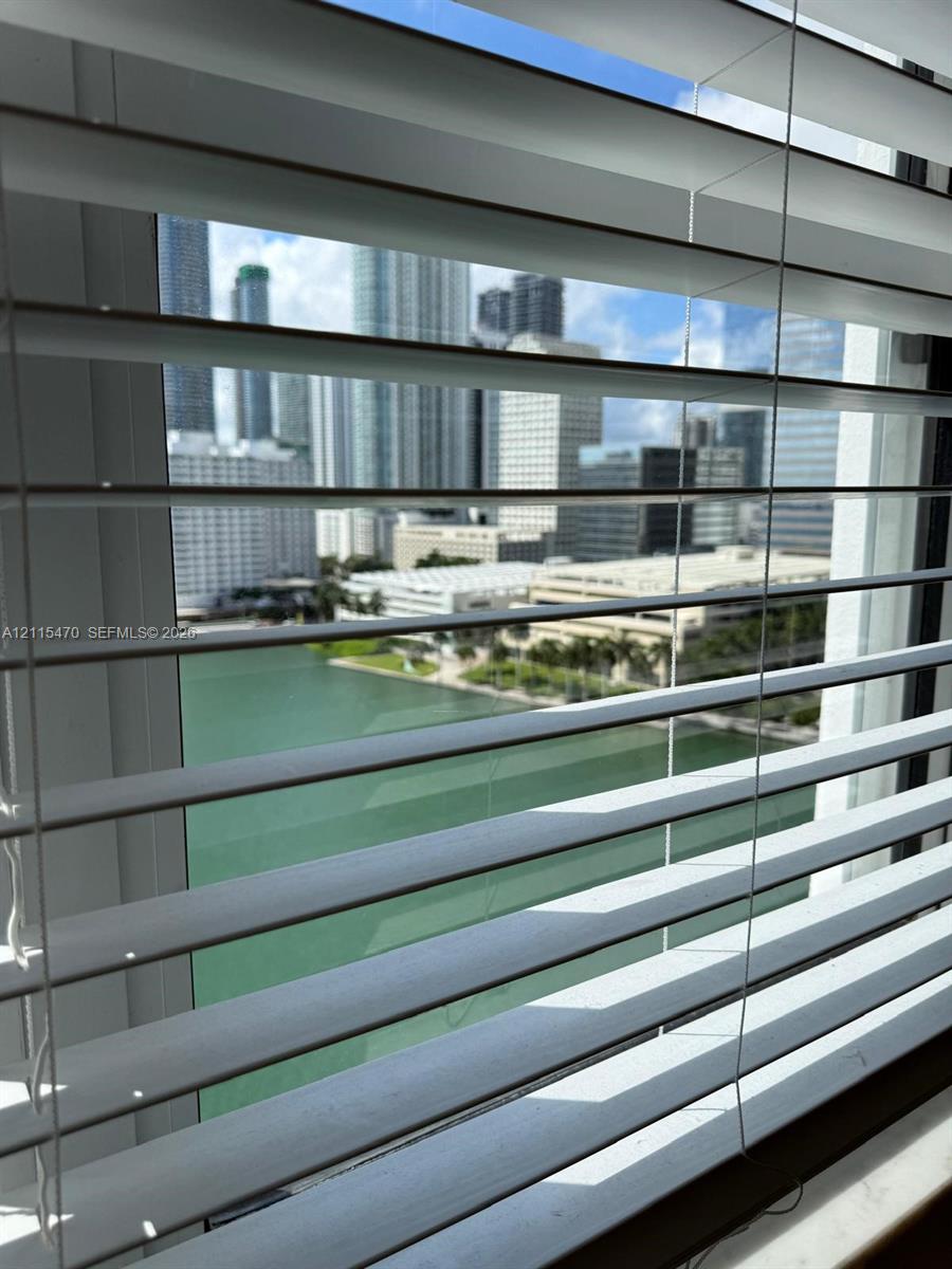 Horizontal white window blinds and a stone window sill featuring a waterway and high-rise skyline backdrop