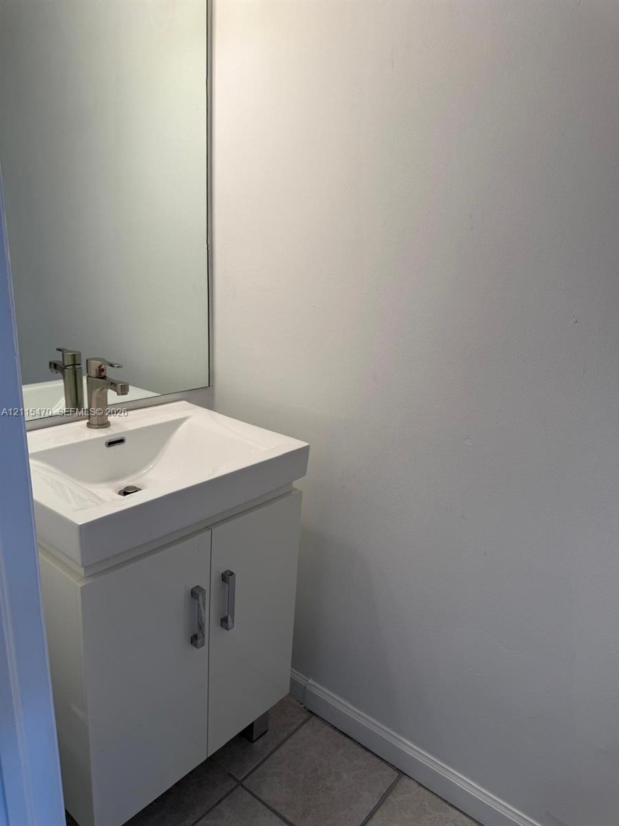 White vanity featuring a rectangular basin, metallic hardware, and an integrated faucet, complemented by a large wall-mounted mirror and neutral tile flooring