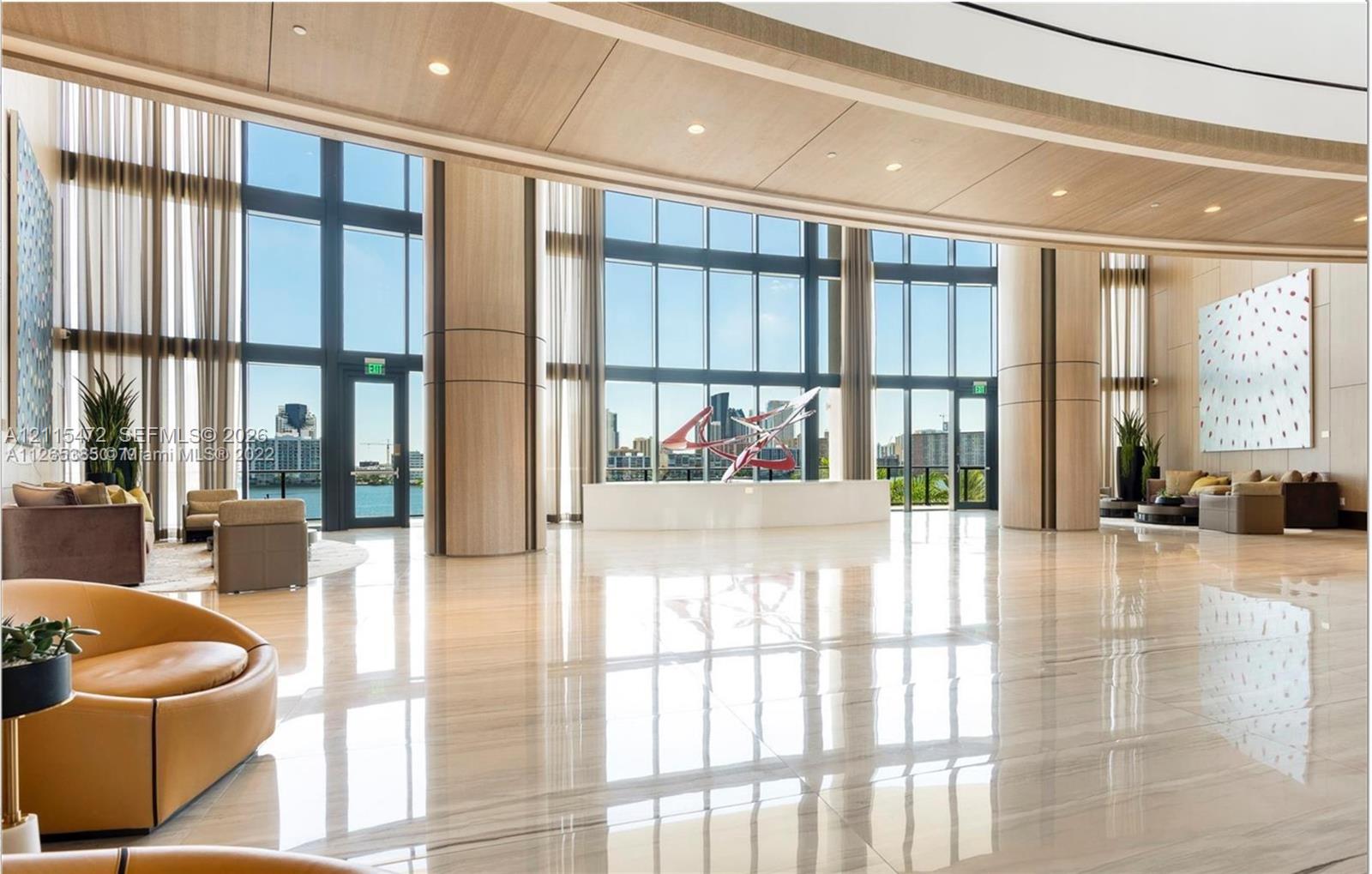 Expansive lobby featuring floor-to-ceiling windows, polished stone flooring, wood-paneled ceiling architectural elements, and recessed lighting