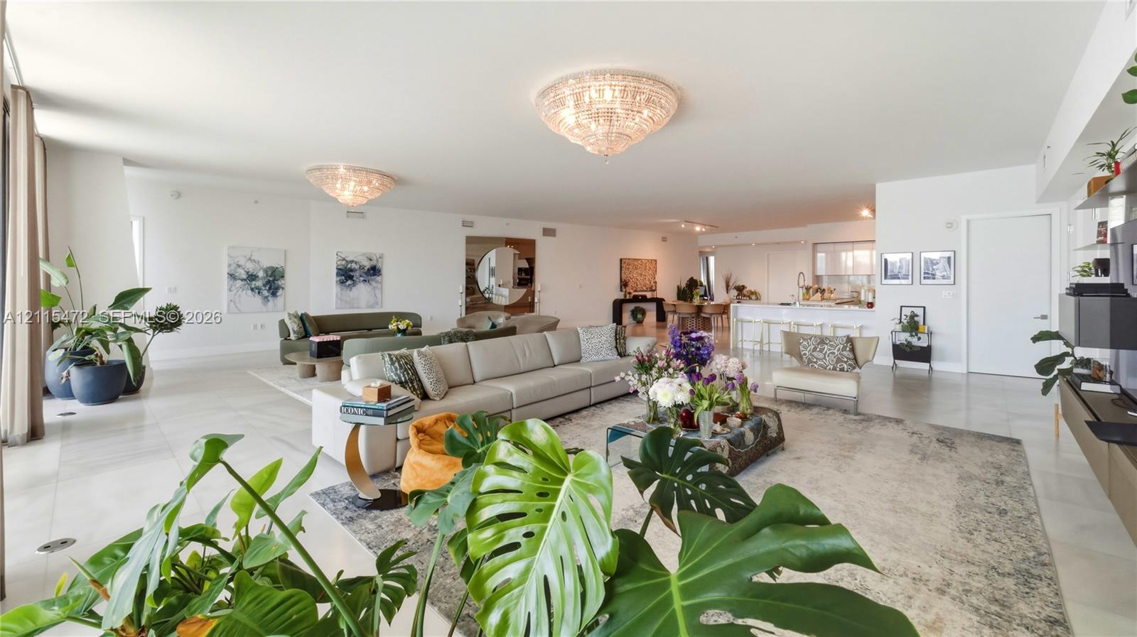 Open-concept living space featuring large-format tile flooring, recessed lighting, ornate crystal flush-mount chandeliers, and a kitchen island with stone-finish countertops