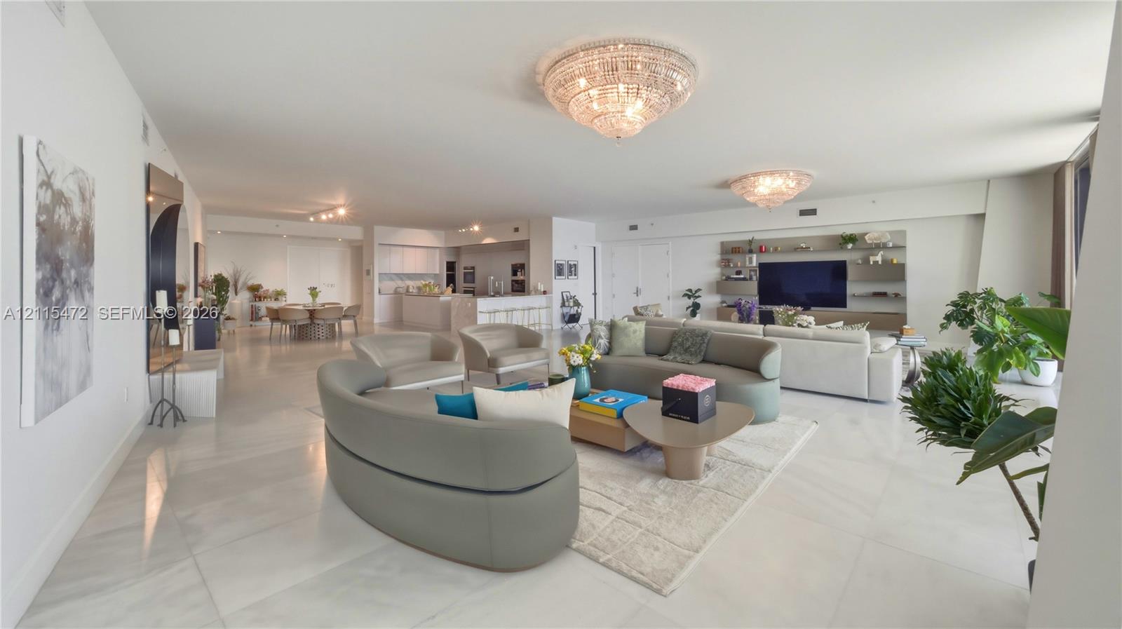 Open-concept living space featuring large-format tile flooring, dual crystal chandeliers, and custom wall-integrated cabinetry