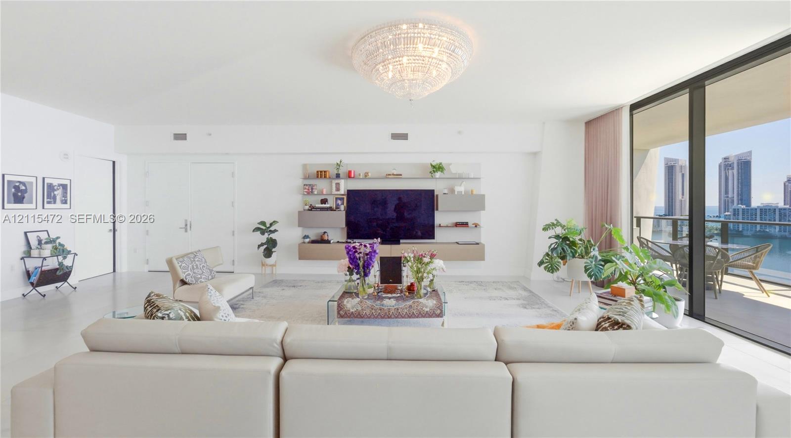 Living area featuring a crystal chandelier, custom wall-mounted shelving unit, expansive floor-to-ceiling glass panels, and a private balcony