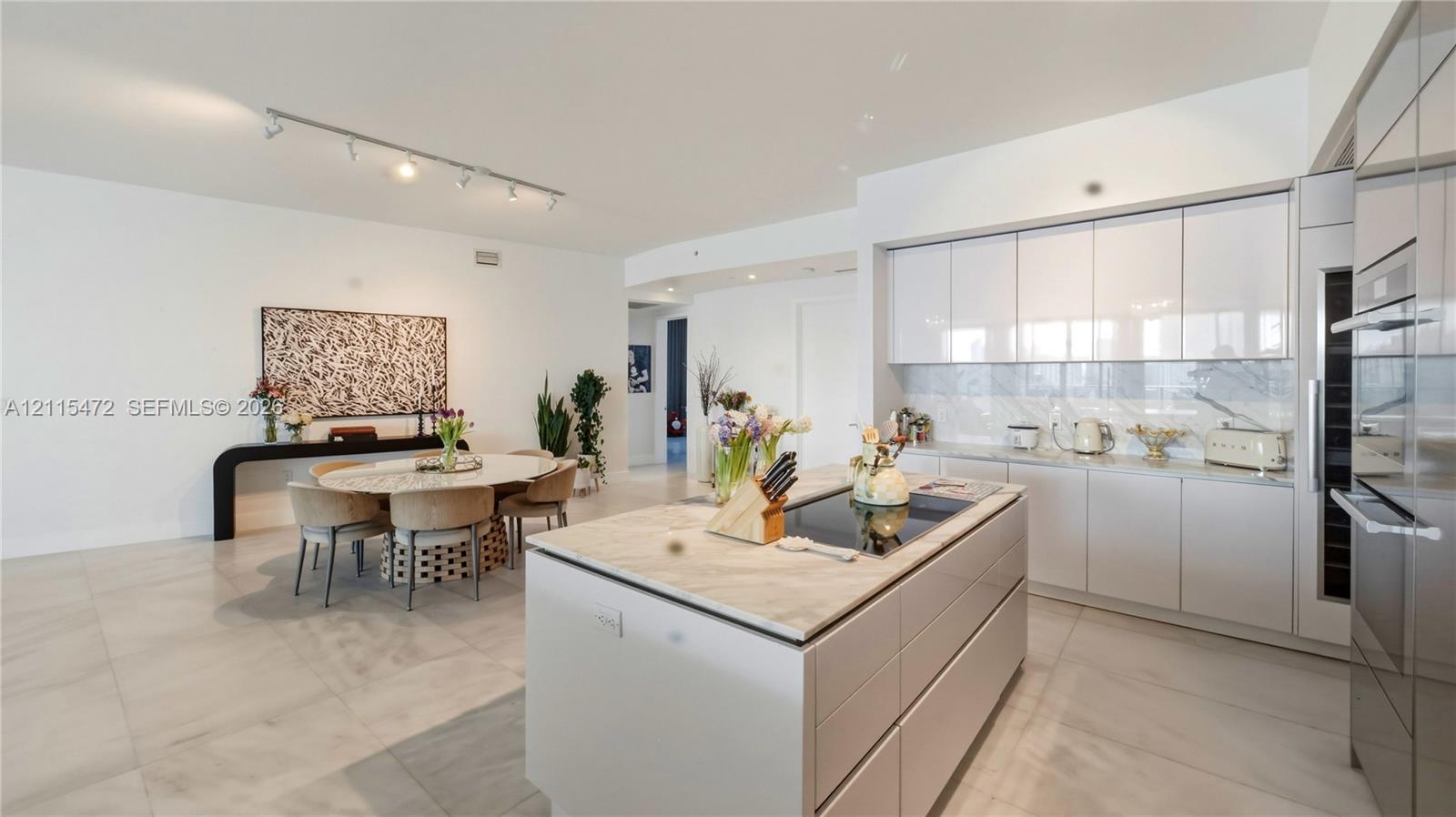 Modern kitchen featuring high-gloss cabinetry, a stone-topped island with a cooktop, integrated stainless steel appliances, and large-format porcelain tile flooring