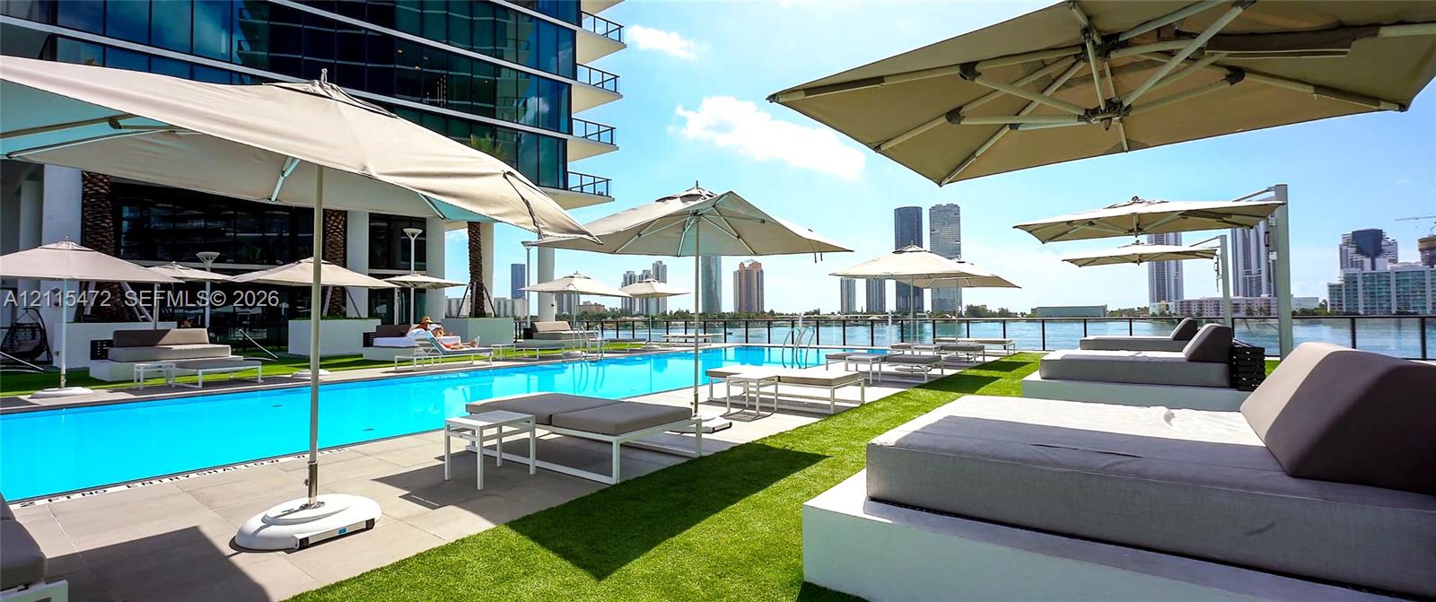 Resort-style lap pool featuring a surrounding stone deck, integrated synthetic turf areas, and water-facing glass railing