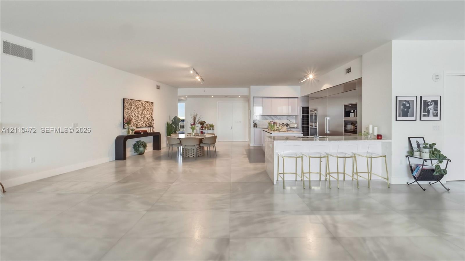 Open-concept interior featuring large-format tile flooring, recessed track lighting, a kitchen island with stone countertops, and built-in stainless steel appliances