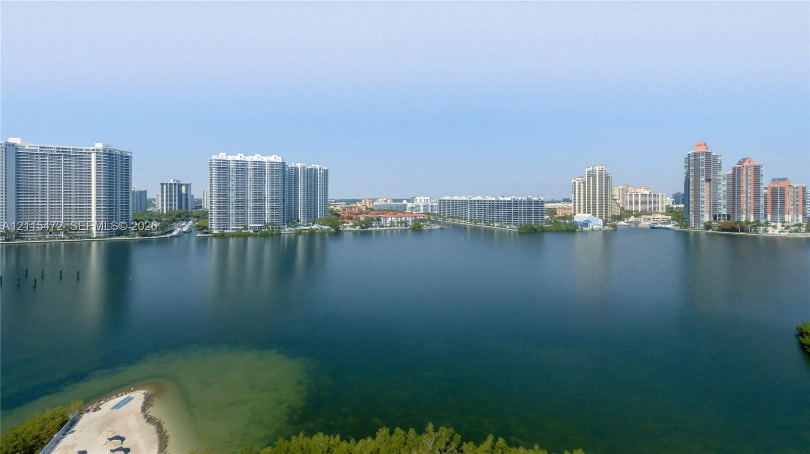 Expansive water frontage featuring a sandy shoreline, natural vegetation, and high-rise surroundings