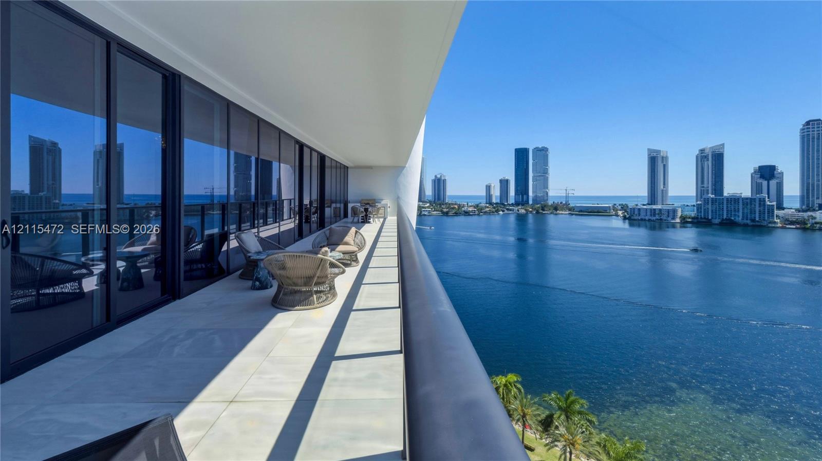 Spacious covered balcony featuring large-format tile flooring, a sleek metal railing, and extensive floor-to-ceiling glass paneling overlooking the bay and skyline Spacious covered balcony featuring large-format tile flooring, a sleek metal railing, and extensive floor-to-ceiling glass paneling overlooking the bay and skyline