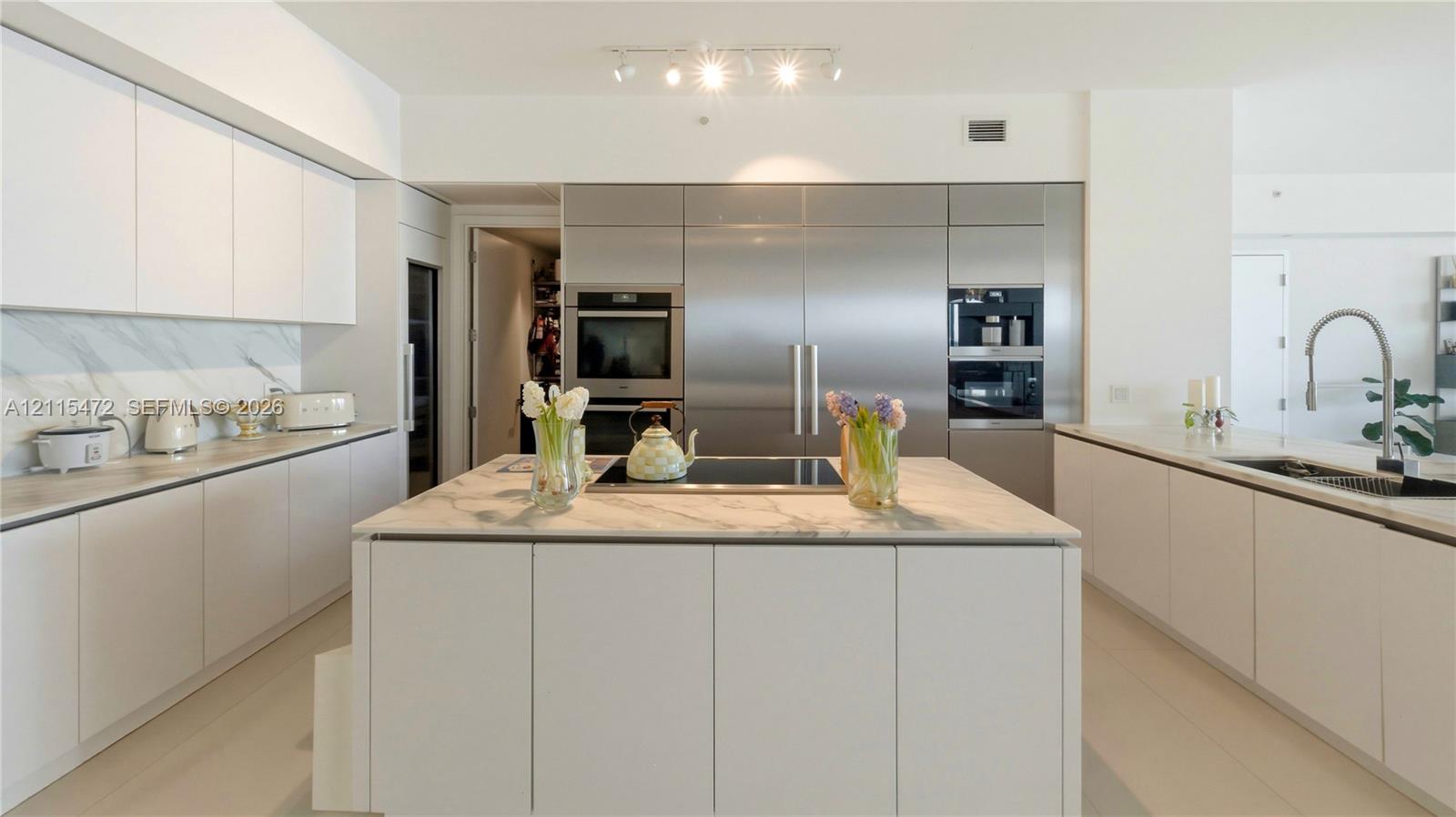 Modern kitchen featuring custom flat-panel cabinetry, integrated stainless steel appliances, a center island with a stone countertop, stone-patterned backsplash, and polished faucet fixtures