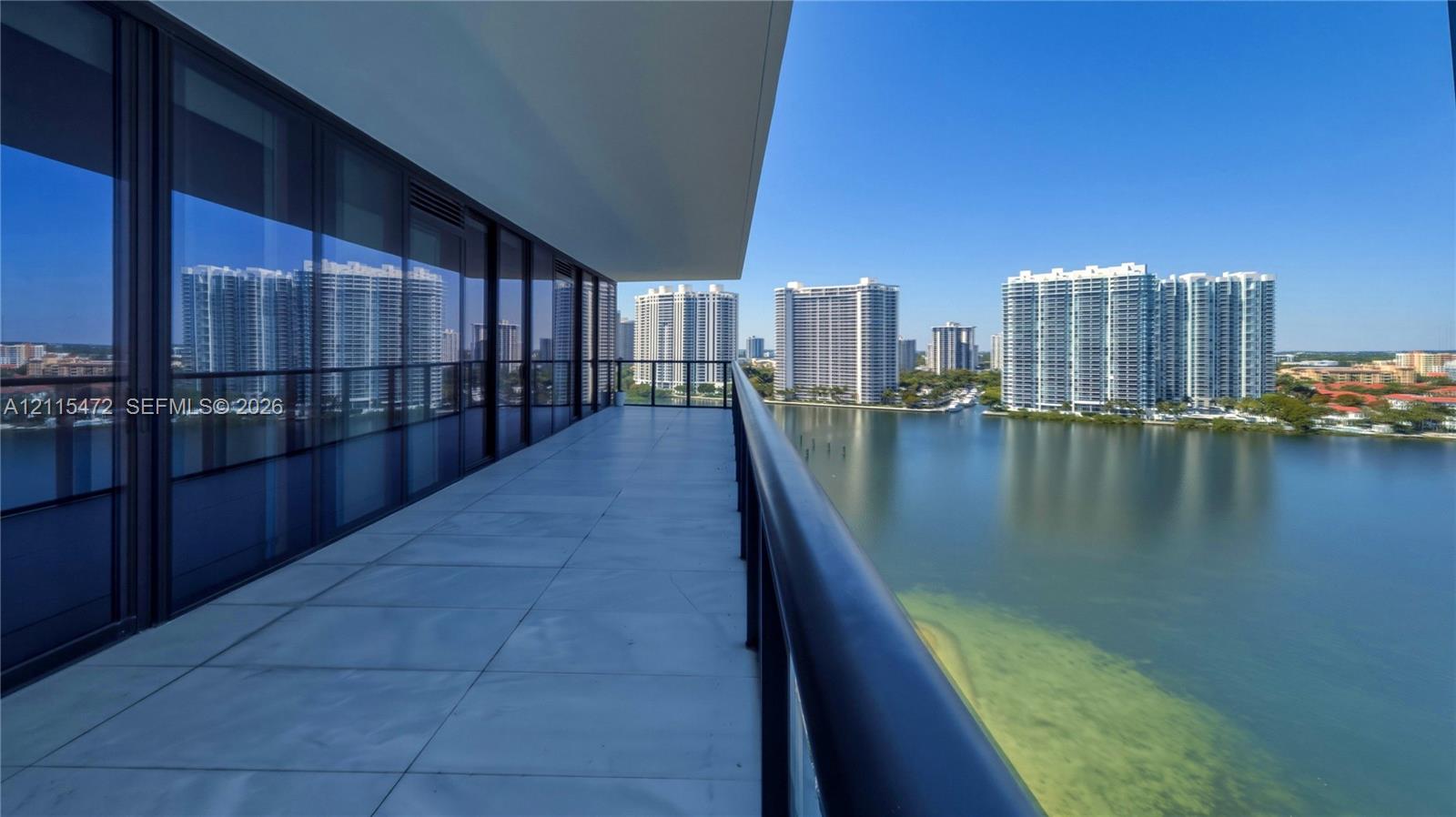 Expansive covered balcony featuring large-format porcelain tile flooring, glass panel railings, and floor-to-ceiling sliding glass walls