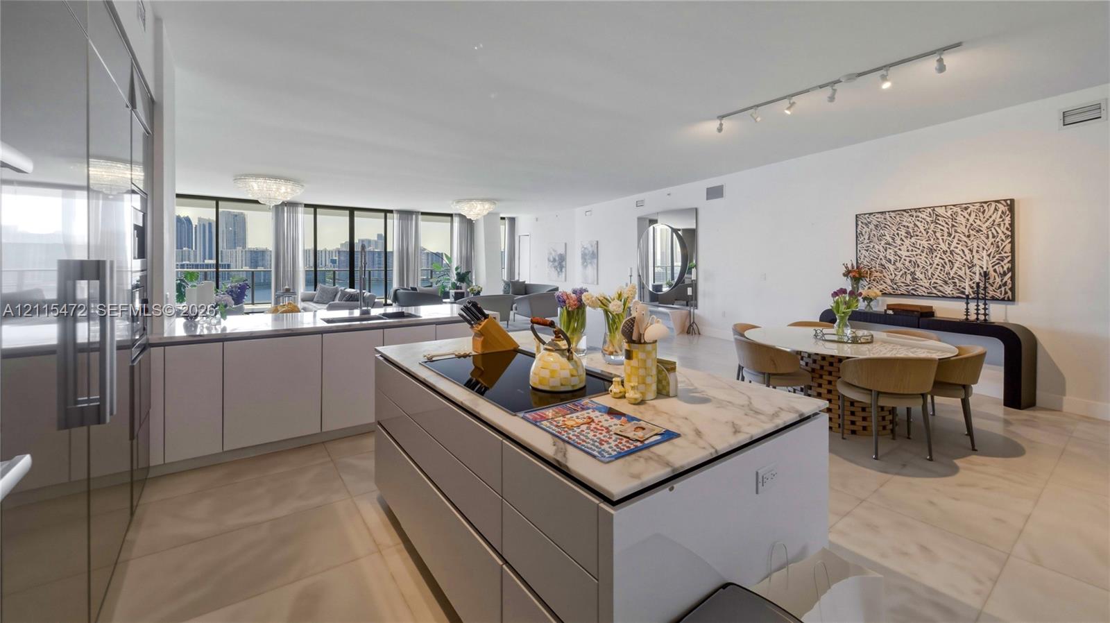Modern kitchen featuring flat-panel cabinetry, a central island with a stone countertop and inset cooktop, floor-to-ceiling windows, and polished tile flooring