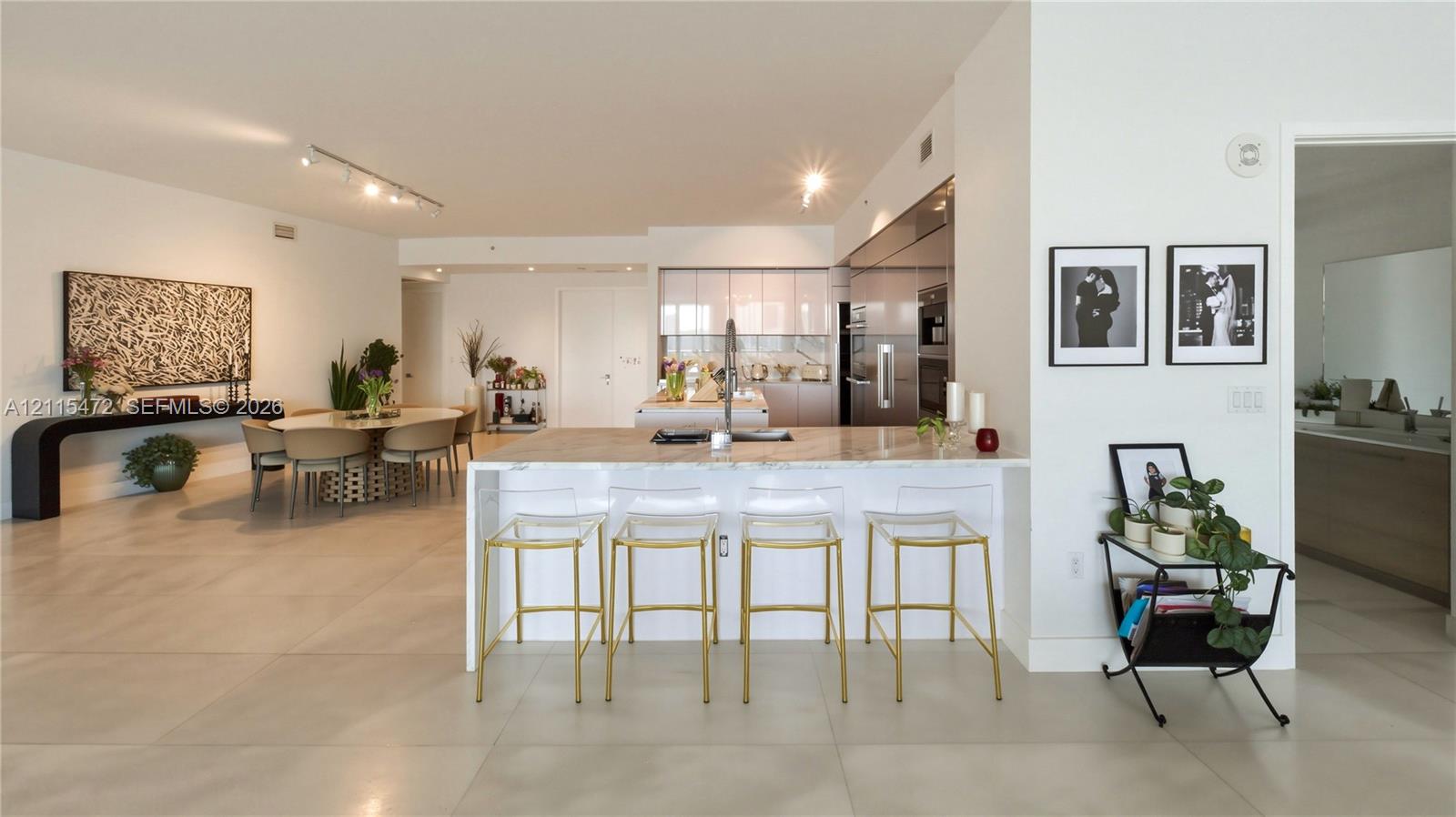Open-concept kitchen featuring an expansive stone-topped island, stainless steel built-in appliances, flat-panel cabinetry, and large-format porcelain tile flooring