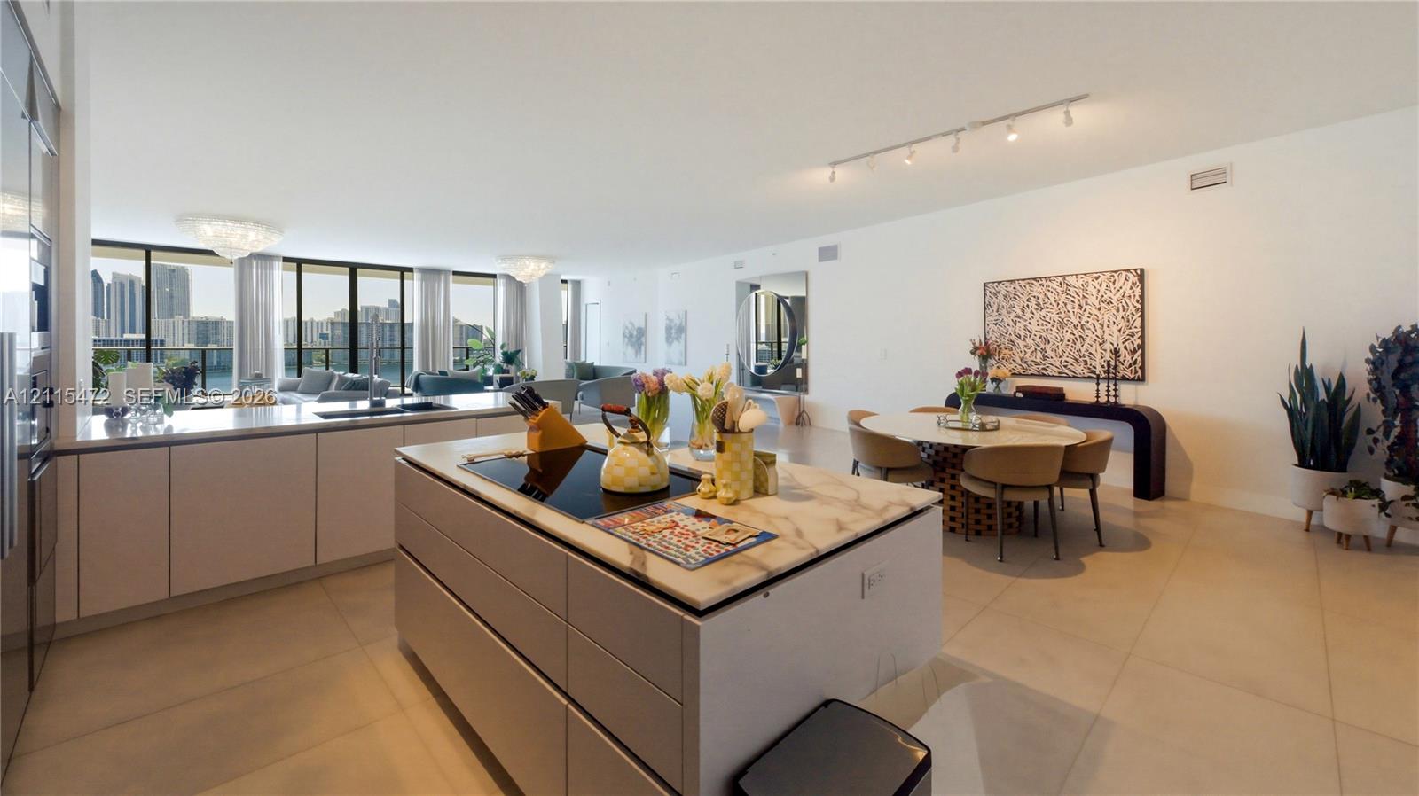 Open-concept living space featuring a central kitchen island with stone countertops, integrated cooktop, large-format tile flooring, and floor-to-ceiling windows