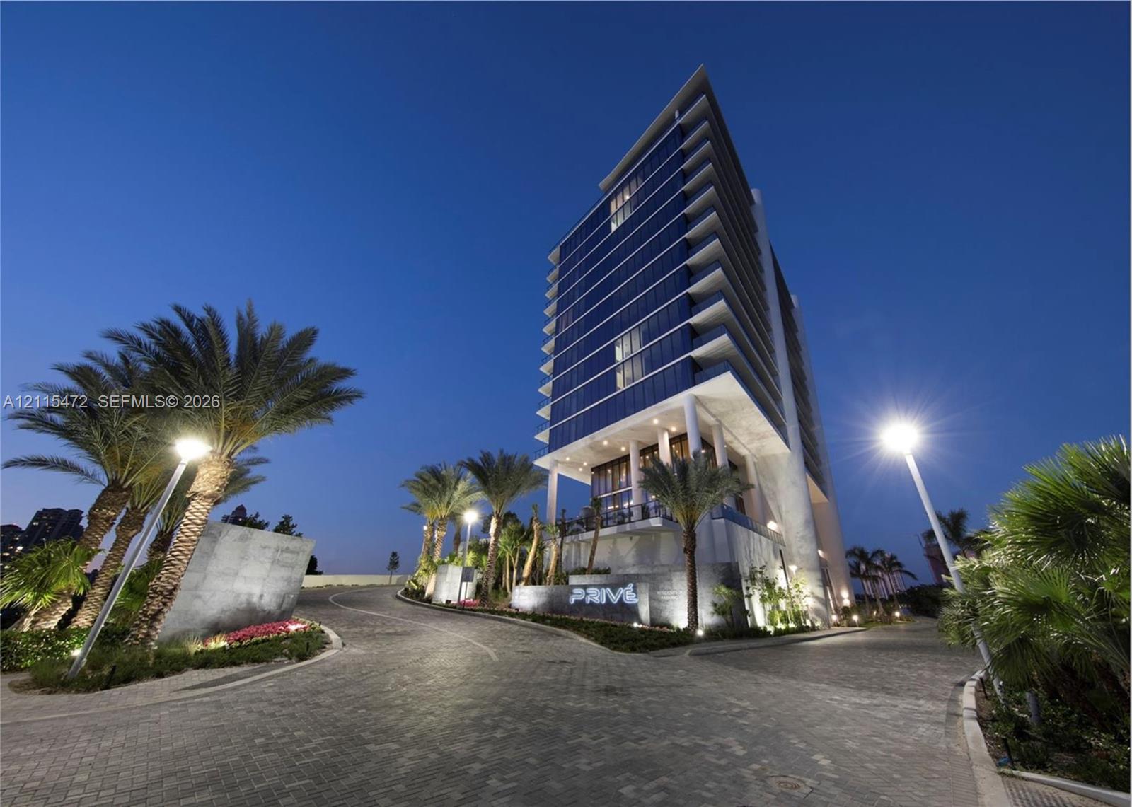 High-rise structure featuring glass curtain walls, cantilevered balconies, stone-paved motor court, and landscaped palms