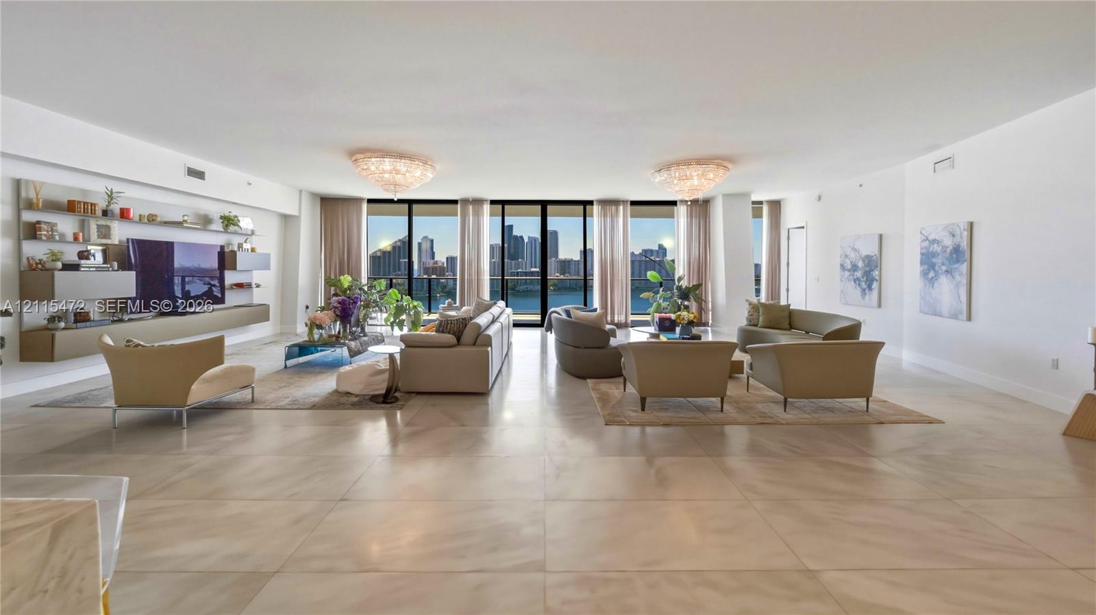 Open-concept interior featuring large-format tile flooring, wall-to-wall floor-to-ceiling windows, custom built-in media shelving, and intricate ceiling-mounted light fixtures