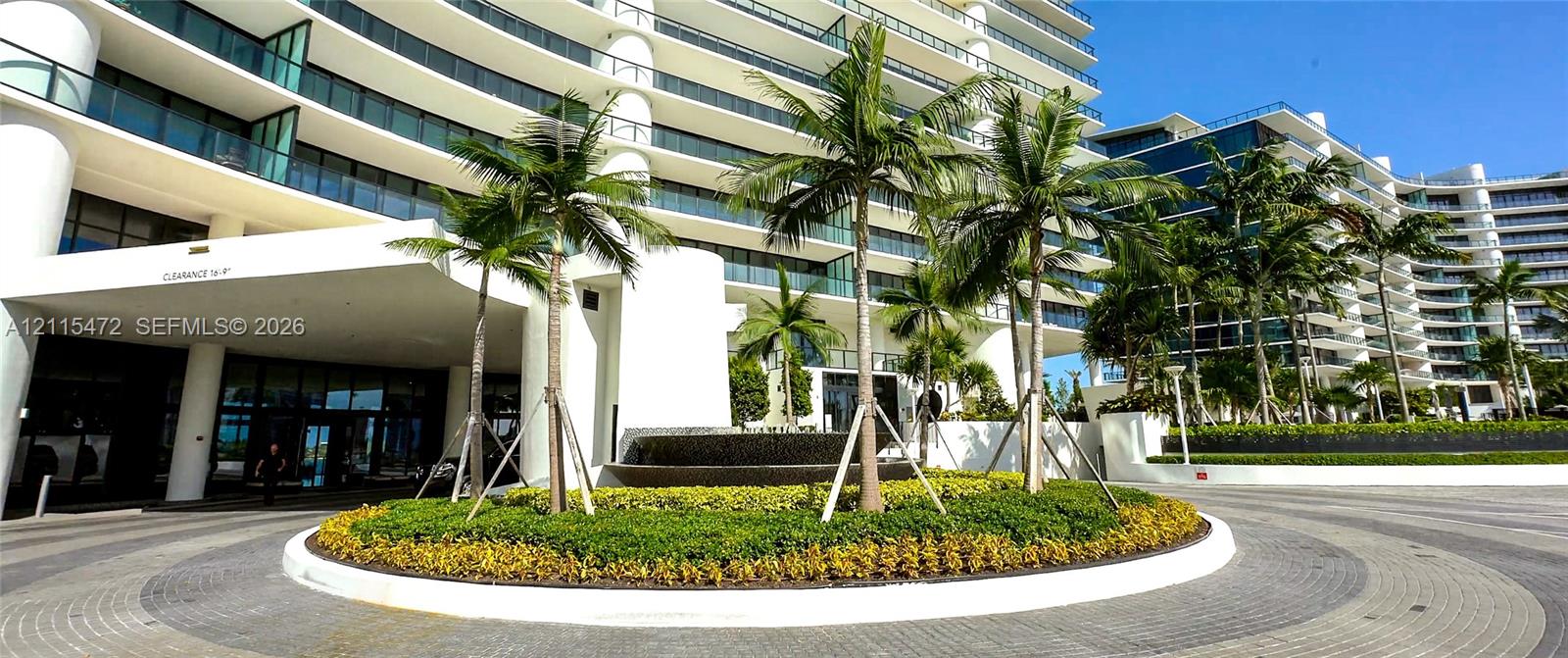 Modern high-rise exterior featuring a circular paved motor court, central landscape island, tiered water fountain, and glass balcony railings