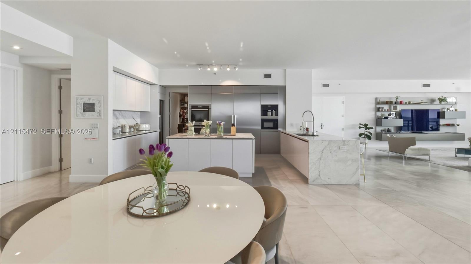 Modern kitchen featuring white flat-panel cabinetry, stone waterfall-edge island, integrated stainless steel appliances, and large-format tile flooring