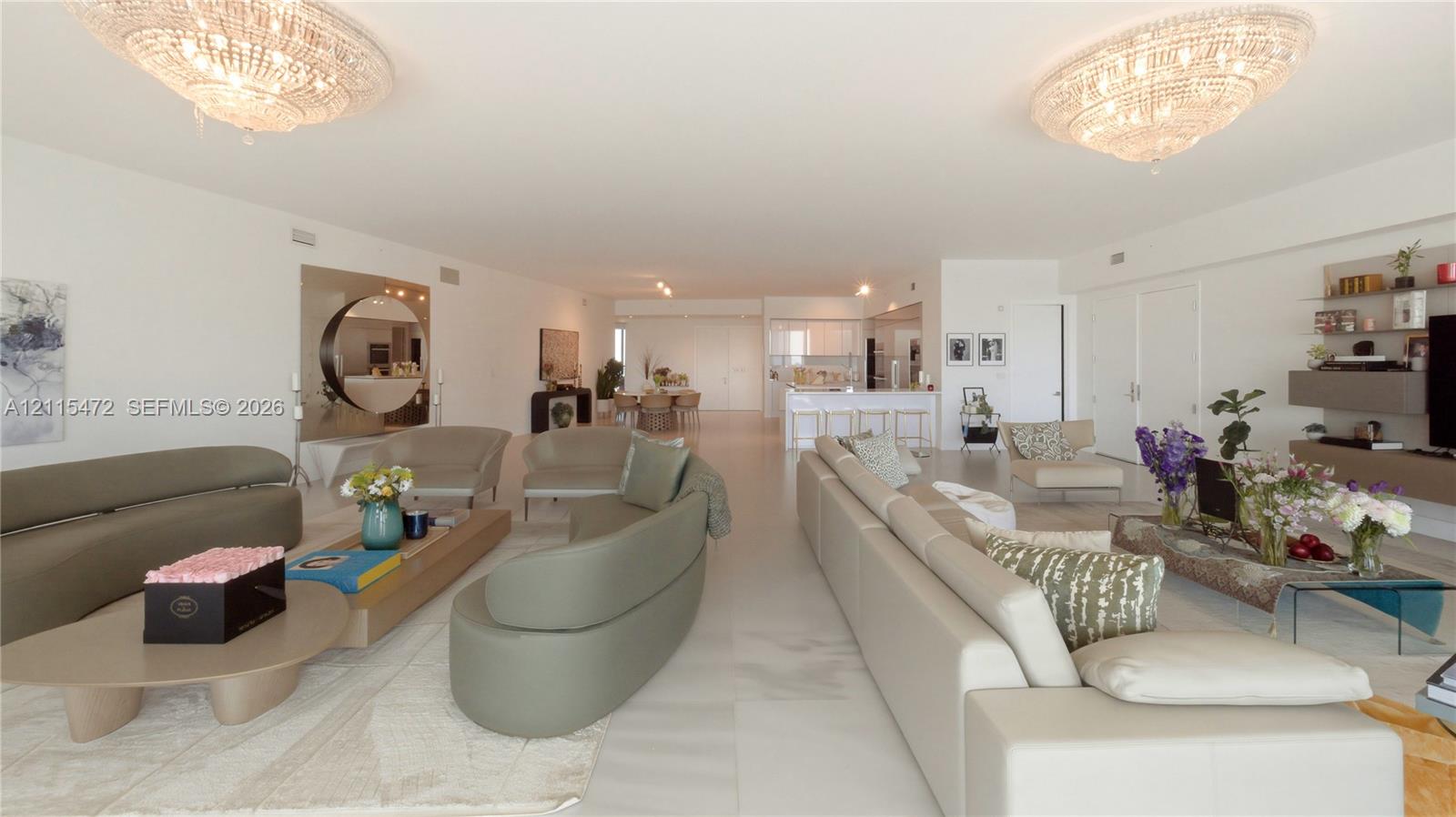 Open-concept interior featuring large-format tile flooring, dual crystal chandeliers, recessed lighting, and built-in wall cabinetry