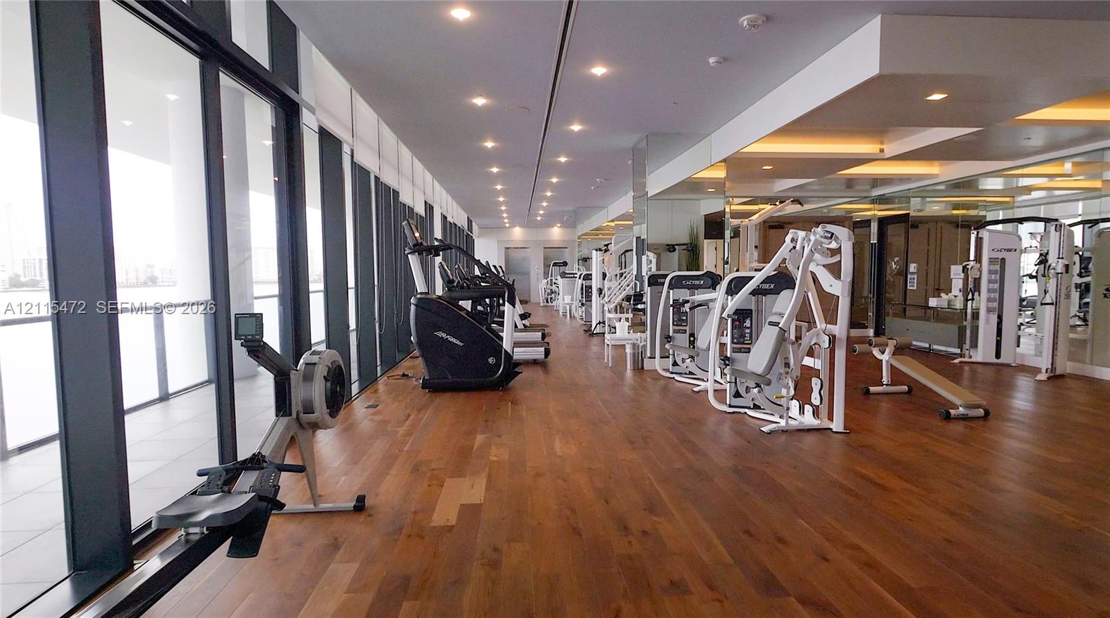 Fitness center featuring wood-finish flooring, floor-to-ceiling windows, recessed lighting, and mirrored walls