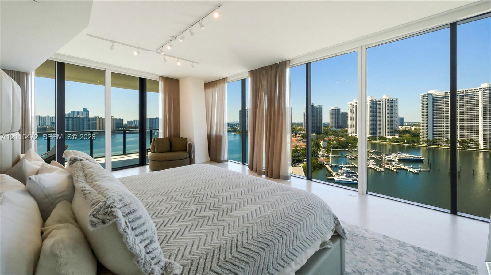 Floor-to-ceiling glass windows, expansive water and skyline scenery, private balcony, and track lighting