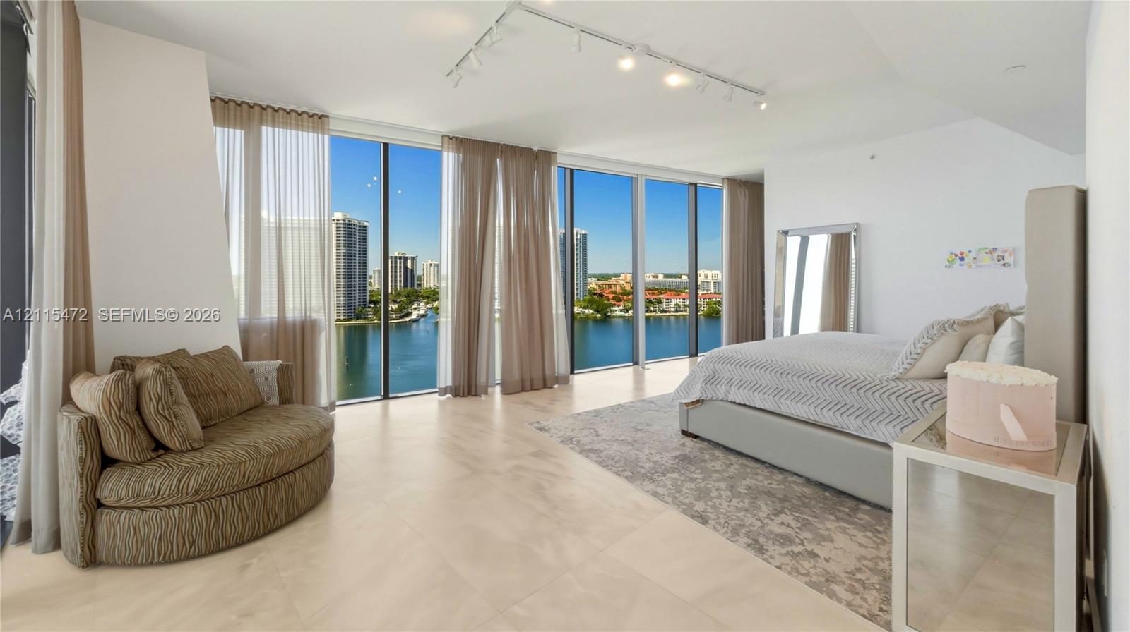 Floor-to-ceiling windows, large-format tile flooring, and track lighting in a room with expansive water and city skyline horizons