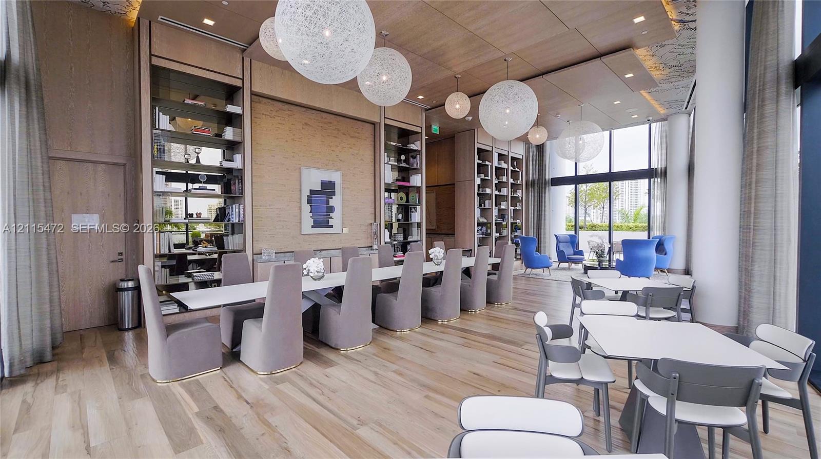 Common area featuring wood-finish flooring, floor-to-ceiling windows, recessed ceiling panels, built-in floor-to-ceiling shelving, and spherical pendant lighting