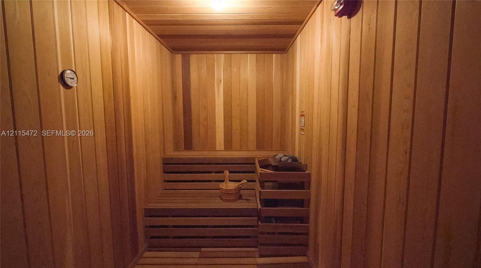 Sauna room featuring tongue-and-groove wood paneling, tiered wood bench seating, and a built-in heating unit with protective wooden enclosure