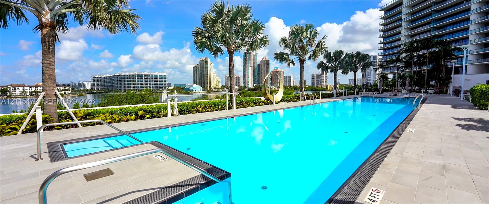Rectangular swimming pool featuring a tiled deck, built-in steps, metal handrails, and surrounding palm trees