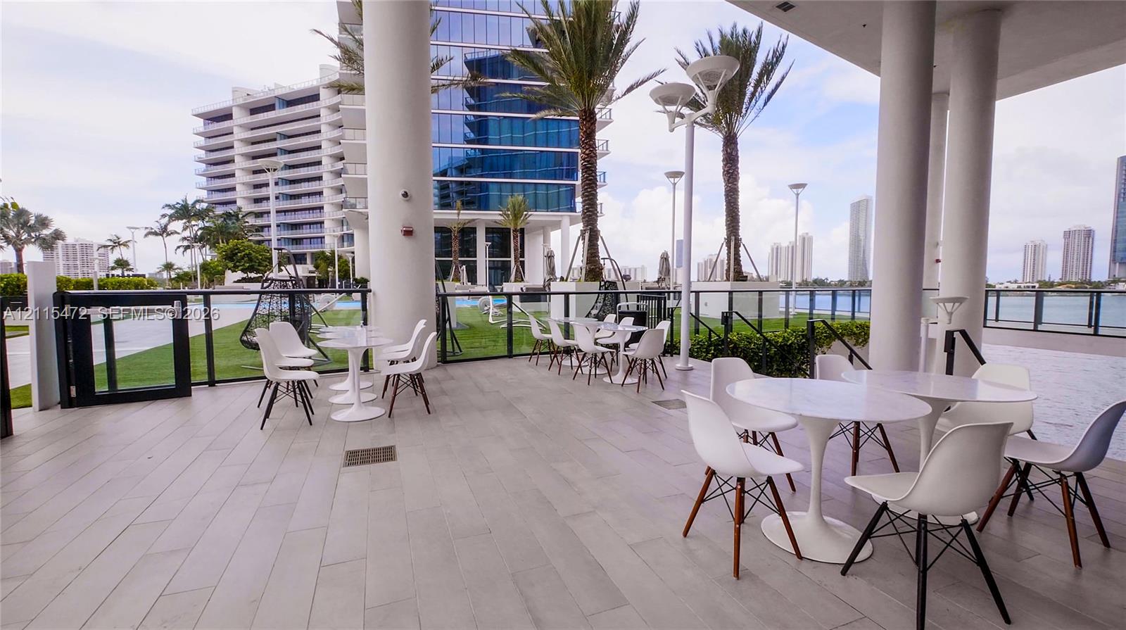 Covered outdoor patio featuring large-format tile flooring, structural pillars, and a glass panel railing system overlooking the water
